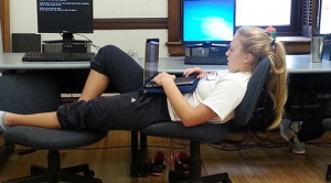 Female student with laptop and stretched across two chairs