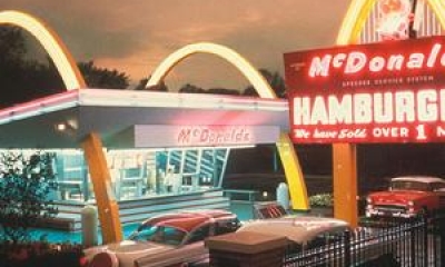 A McDonalds restaurant in 1955 with bright lights and 50's era cars