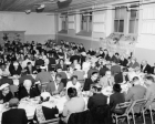 black and white photo of large group of people at tables in a hall