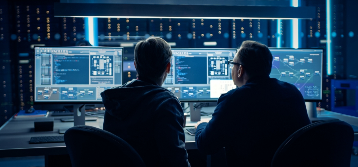 Two Professional IT Programers Discussing Blockchain Data Network Architecture Design and Development Shown on Desktop Computer Display. Working Data Center Technical Department with Server Racks