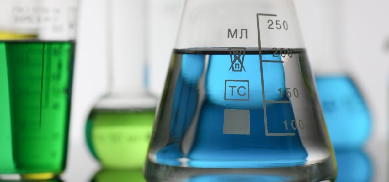 close up image of multiple beakers filled with blue and green liquid