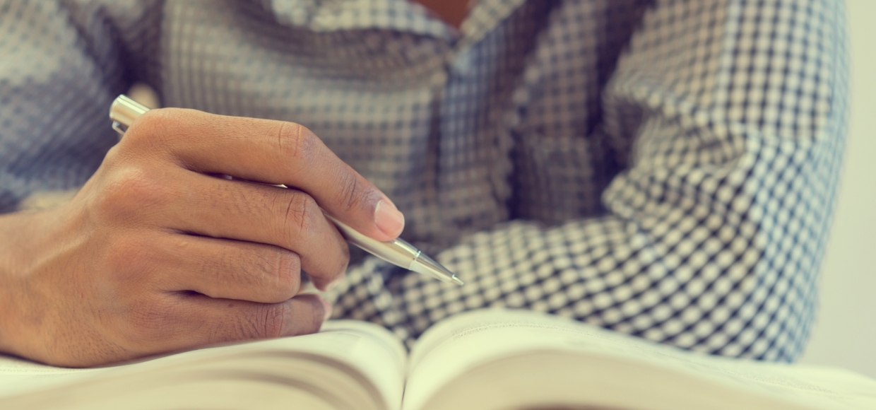 close up student man hand holding pen for guideline reading on text book at campus library for examination education concept
