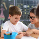 Children drawing with smiling preschool teacher assisting them. You can get an education masters at CHC and learn to harness creativity and support.