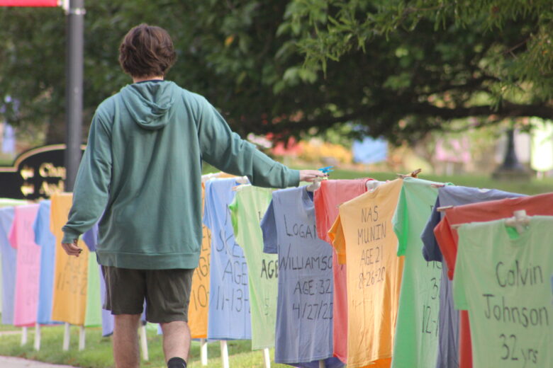 student walking by t-shirt memorial in honor of the Institute for Forgiveness and Reconciliation Week of Nonviolence