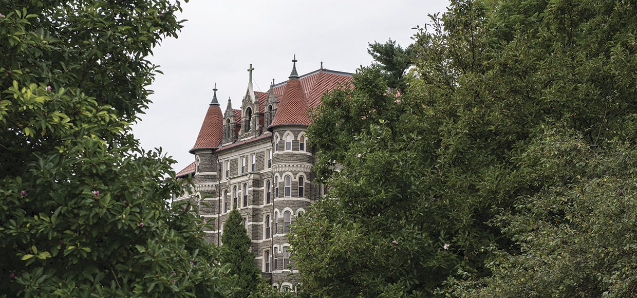 View of Saint Joseph Hall, a stone building with terra cotta roof tiles, through the trees