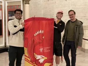 two students holding Chestnut Hill College flag with professor