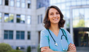 Young woman in blue scrubs with a stethoscope around her shoulders, smiling at the camera