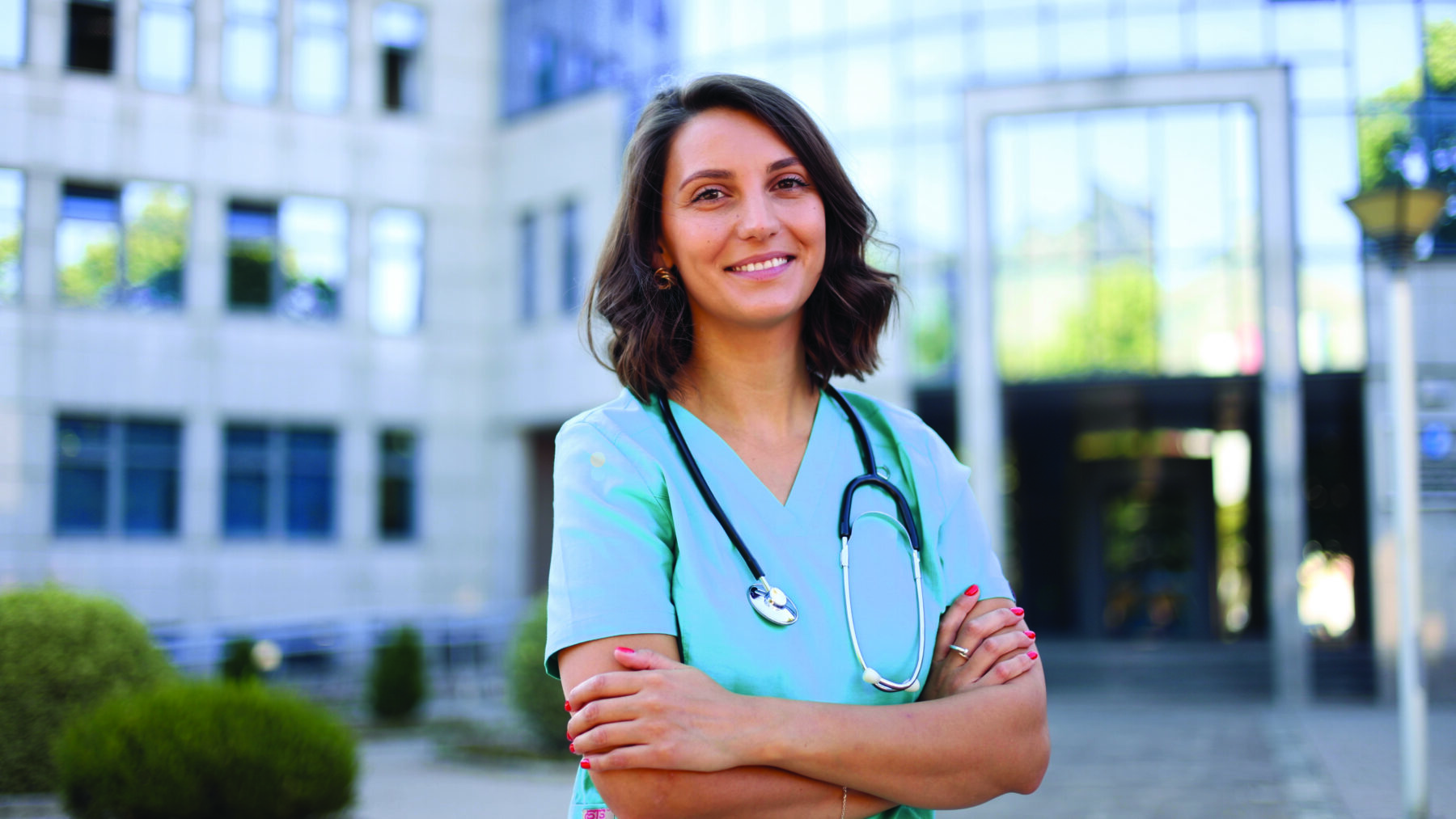 Young woman in blue scrubs with a stethoscope around her shoulders, smiling at the camera