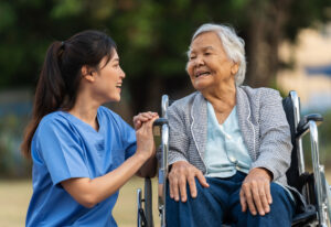 Happy nurse take care and talking with senior woman patient in wheelchair at park