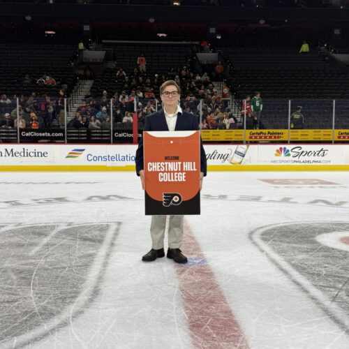 male stands on the ice at a Flyers game, posing with sign