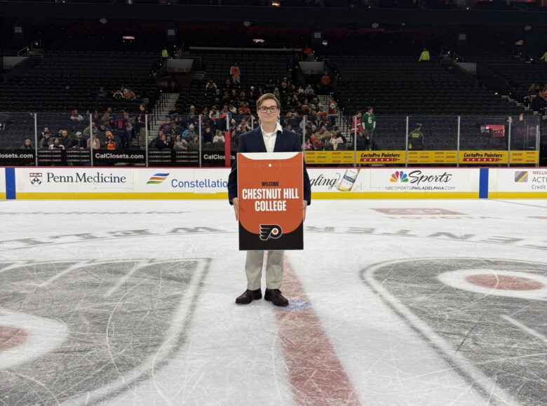 male stands on the ice at a Flyers game, posing with sign