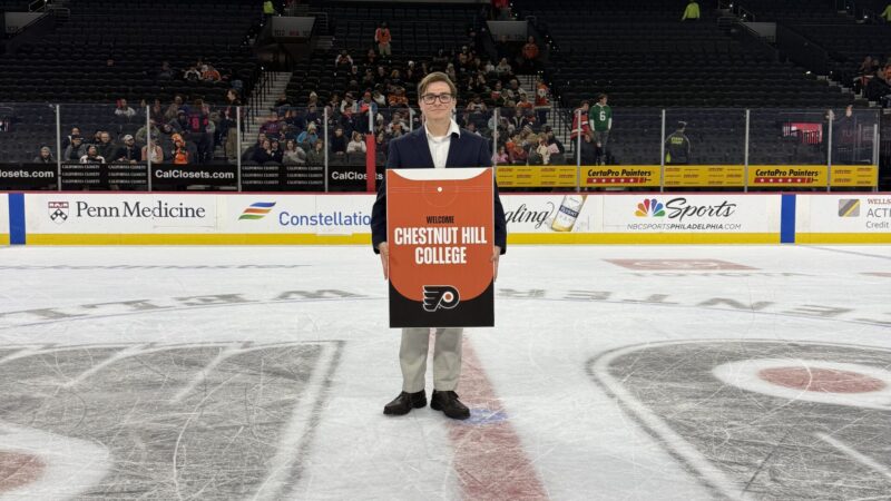 male stands on the ice at a Flyers game, posing with sign