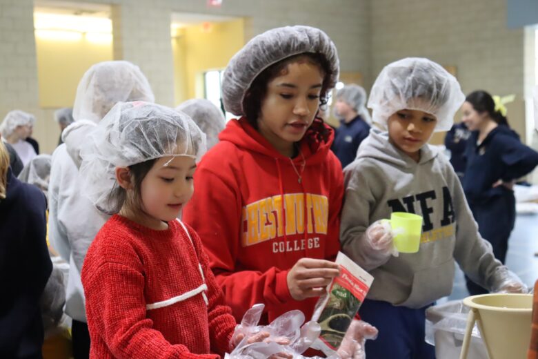 older female student works with two younger students on a service project bagging rice.