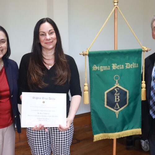three individuals smiling as a woman receives an award