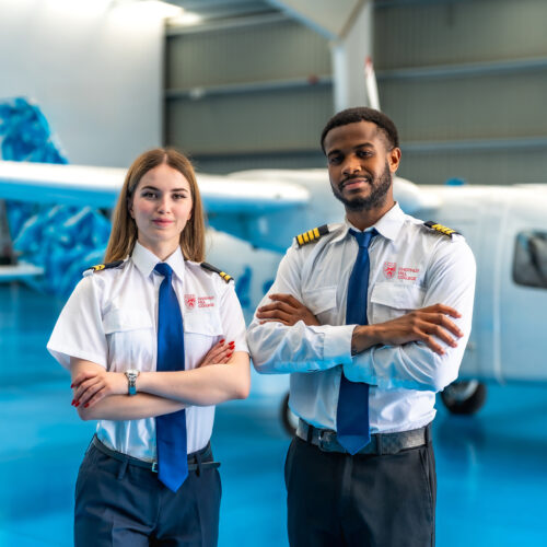 two pilots stand in front of a plane inside an aircraft hangar