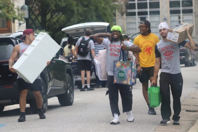 male students moving furniture and items into dorms while standing outside.